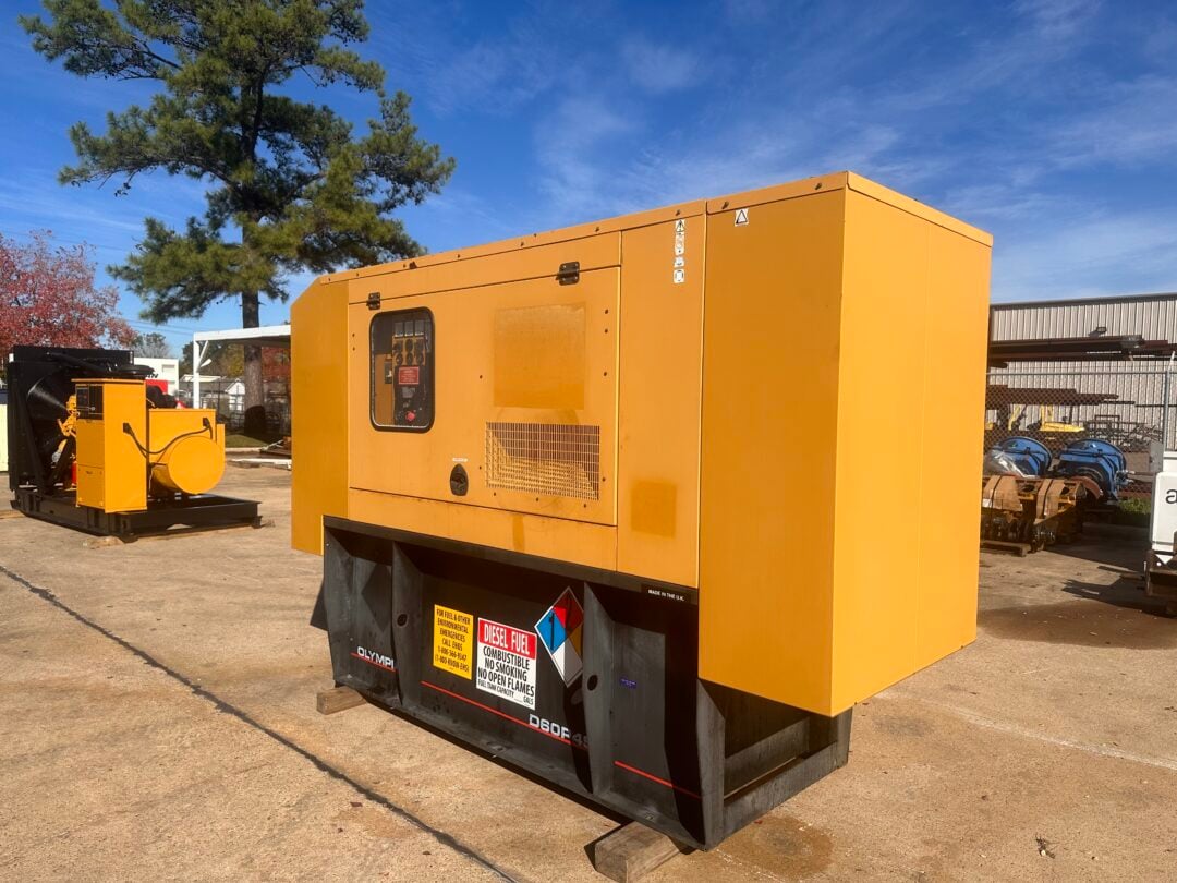 Large yellow diesel generator on a trailer outdoors, with warning labels and a control panel visible against a blue sky and trees.